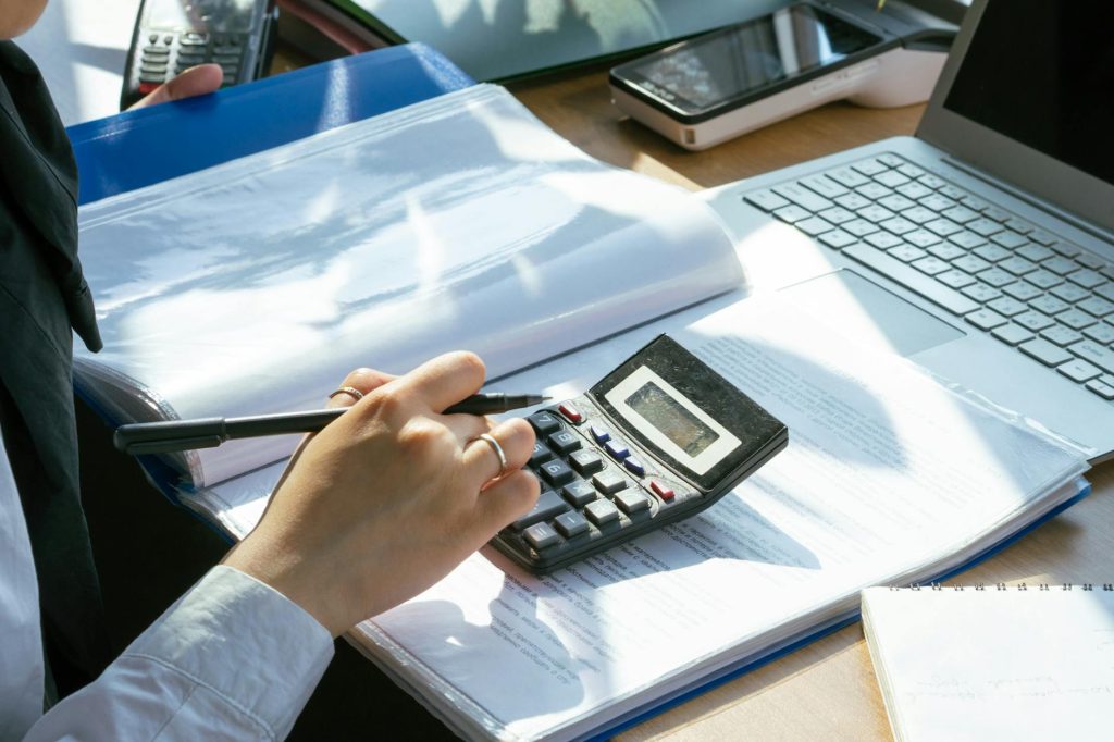 Moving Large Office Equipment: Effortless Budget Hacks A person working on financial calculations using a calculator and laptop at an office desk.