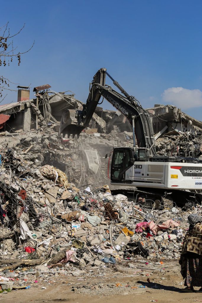 Excavator working among rubble in ruins on a clear day, symbolizing reconstruction.
