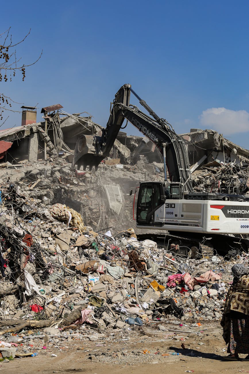 Excavator working among rubble in ruins on a clear day, symbolizing reconstruction.