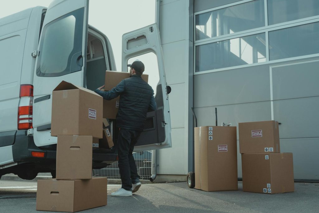 Safe Transport: 3 Must-Have Pro Tips for Packing Your Car A delivery man unloading cardboard boxes from a van at a warehouse during the day.