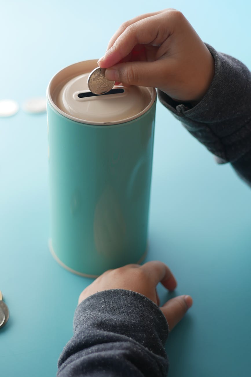 Child's hands putting a coin into a sleek blue piggy bank on a table.