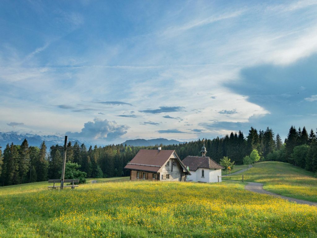 Affordable House Removals: 3 Must-Know Secrets for Effortless Moves Charming Swiss countryside scene featuring a farmhouse and chapel amidst lush green fields and forests.
