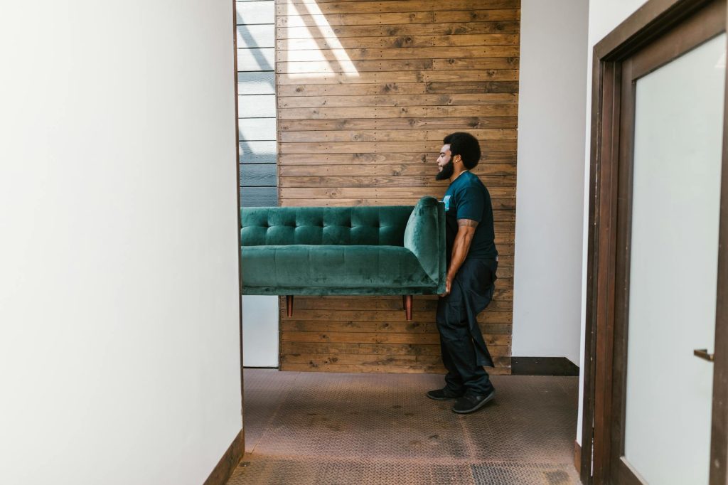 Moving Heavy Appliances Without Hassle: Top 3 Expert Tips A mover carries a green sofa indoors, showcasing modern interior design and relocation services.
