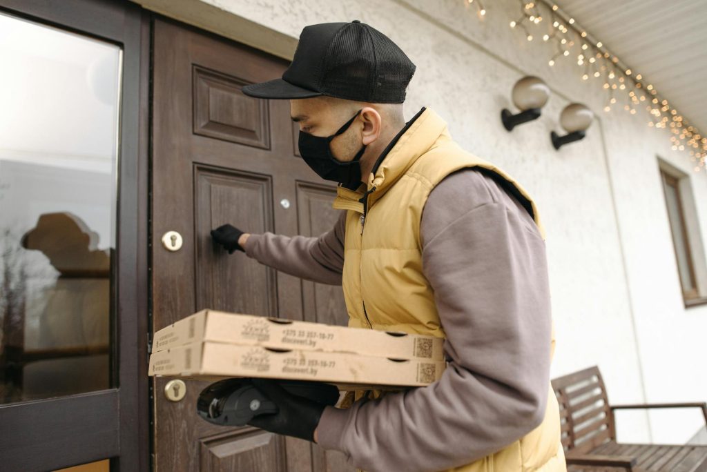 House Removal Day: 4 Essential Checks for a Stress-Free Move A deliveryman wearing a mask and gloves knocks on a door while holding pizza boxes, emphasizing safety during delivery.