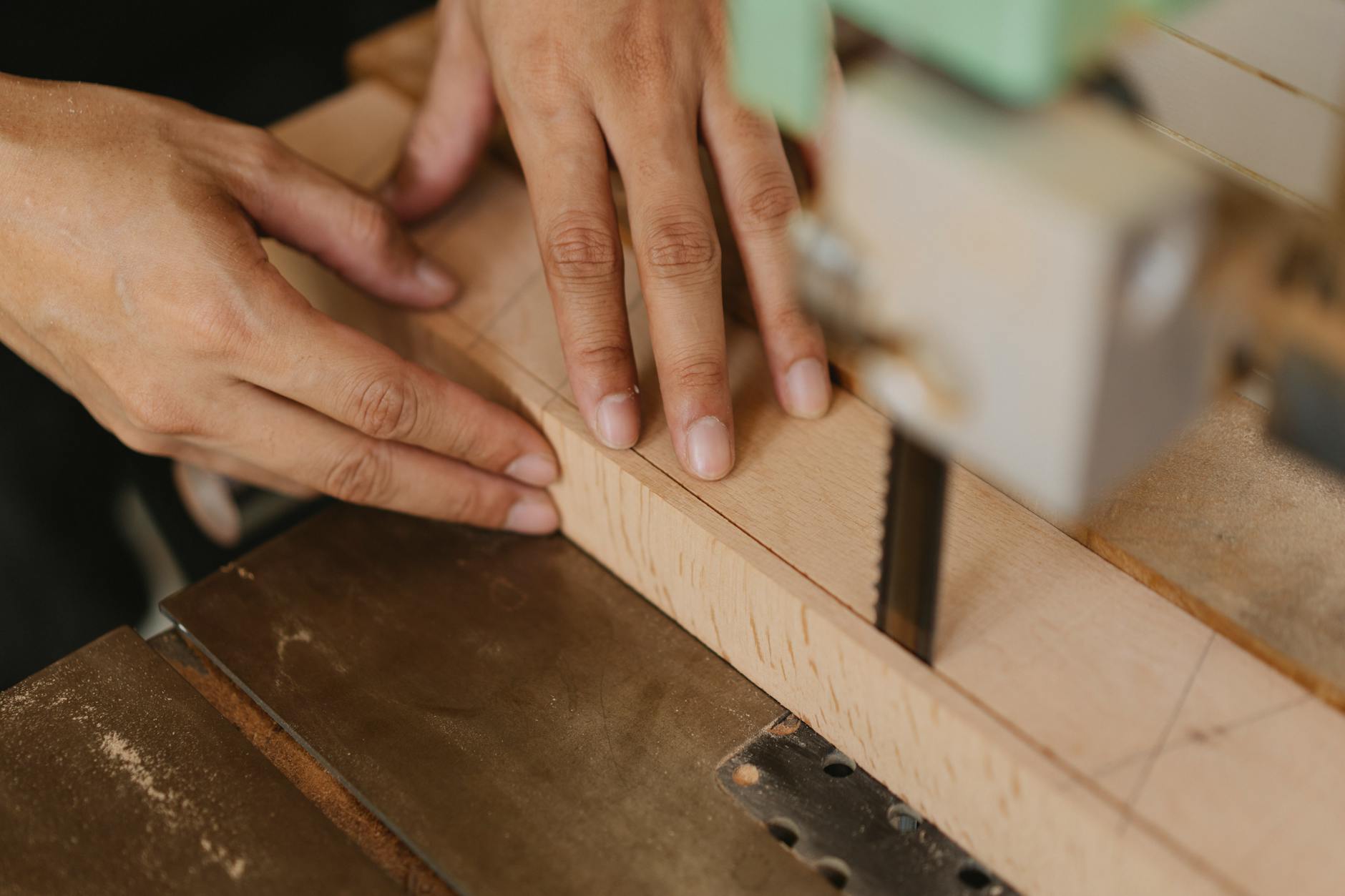Industrial Equipment Moves: Effortless Cost-Cutting Strategies Close-up of hands guiding wood through a band saw, showcasing craftsmanship and precision.