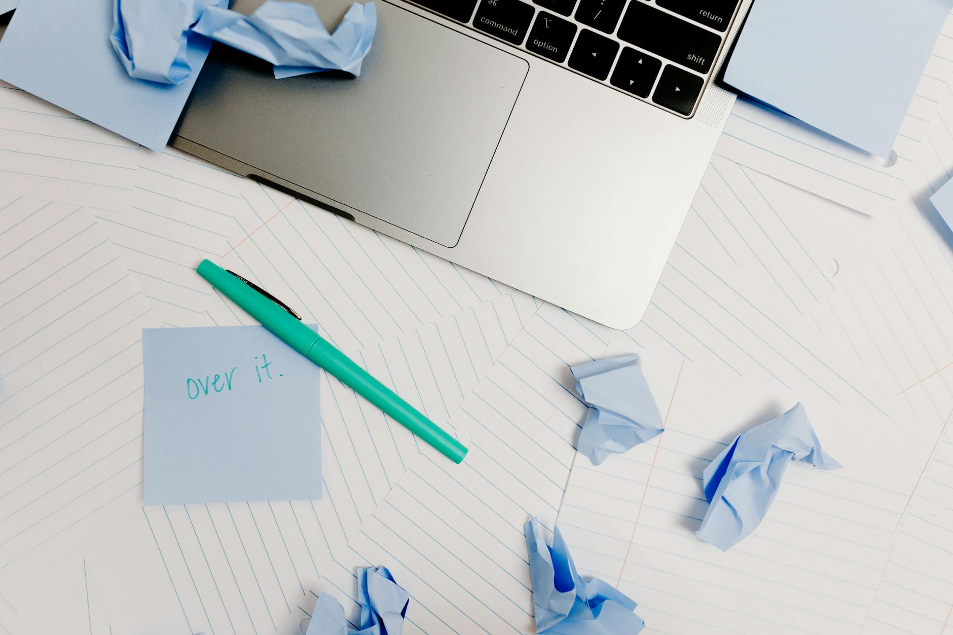 Effortless Waste Pickup: 4 Powerful Tips for Stress-Free Planning A messy desk with a laptop, post-it note saying 'over it,' and crumpled notes symbolizing burnout.