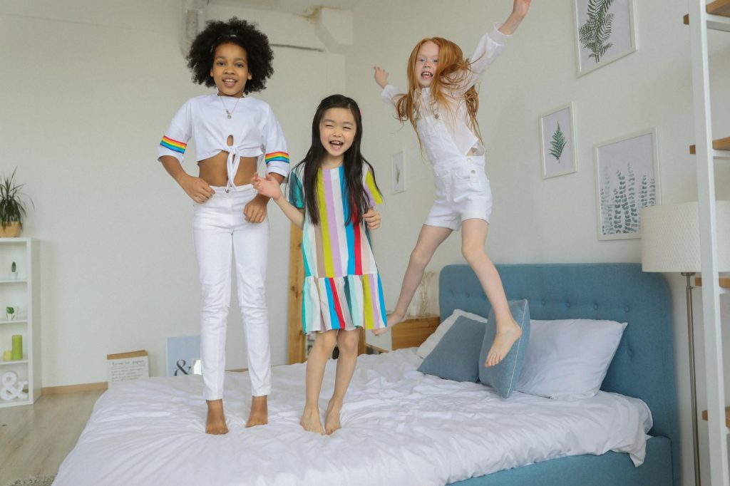 Budget-Friendly: 5 Must-Try Hacks for Your Next Home Move Three cheerful girls jumping on a bed, showcasing vibrant energy and joy in a cozy indoors setting.