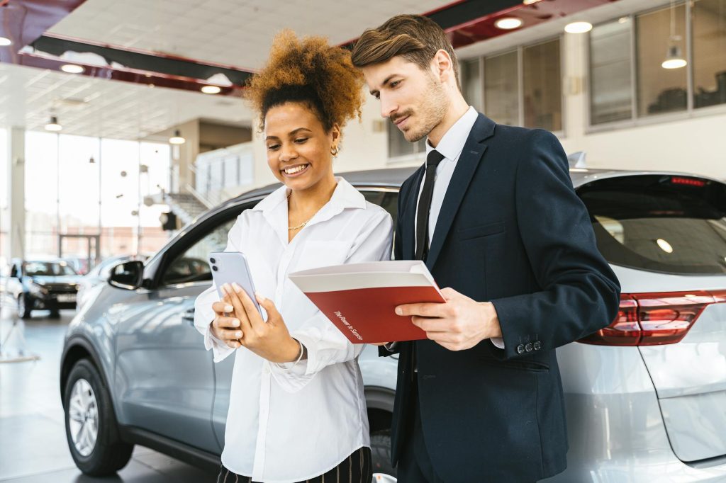 Budget-Friendly: 5 Must-Have Options for Effortless Cross-Country Car Moves A woman and man smiling while reviewing details at a car dealership. Perfect for business or lifestyle imagery.