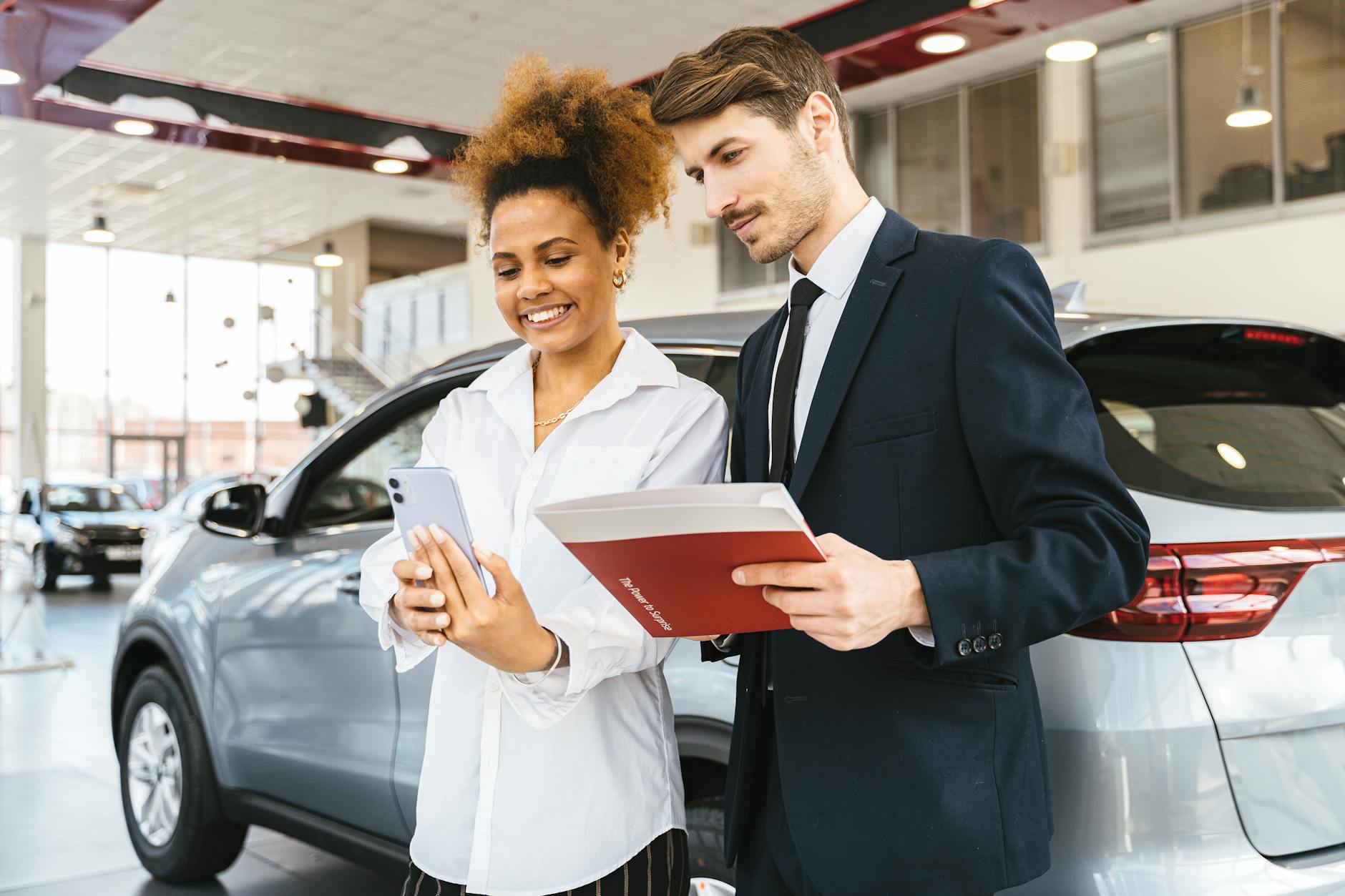 Budget-Friendly: 5 Must-Have Options for Effortless Cross-Country Car Moves A woman and man smiling while reviewing details at a car dealership. Perfect for business or lifestyle imagery.