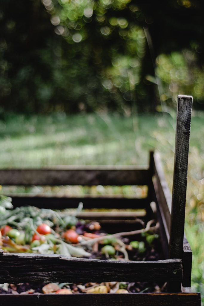 Close-up of a wooden compost bin with organic waste in a lush garden setting.