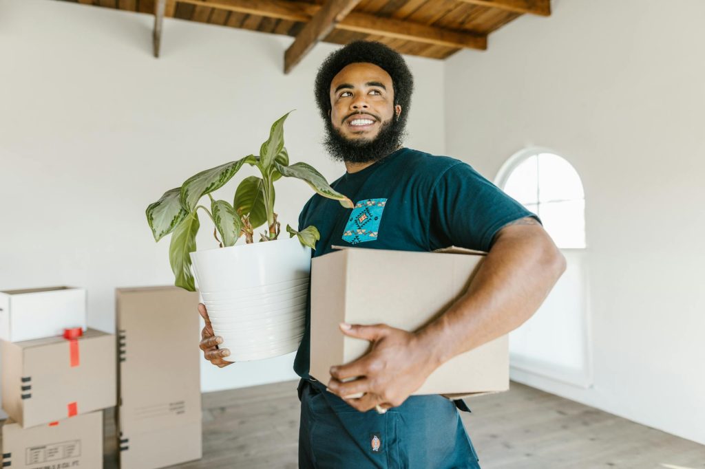F1 Removals: Top 5 Reasons to Choose for Effortless Home Move Smiling man holding a moving box and potted plant in a bright new home.