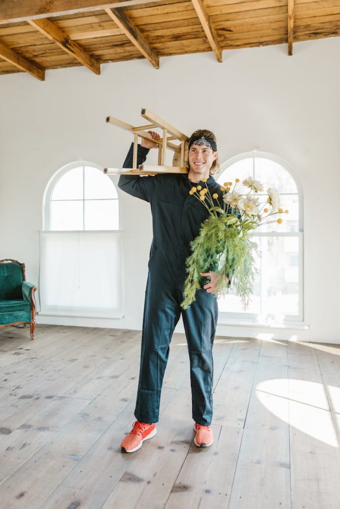 Budget-Friendly DIY Moving: 5 Salvage Hacks for Effortless Moves A man in work overalls moves a chair and flowers into a bright new home.