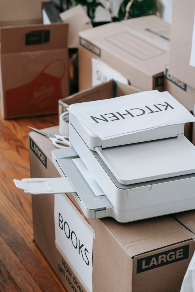 Declutter Your Office Before a Move: 5 Effortless Tips A collection of large cardboard boxes labeled for moving, alongside a printer, representing organization and preparation indoors.