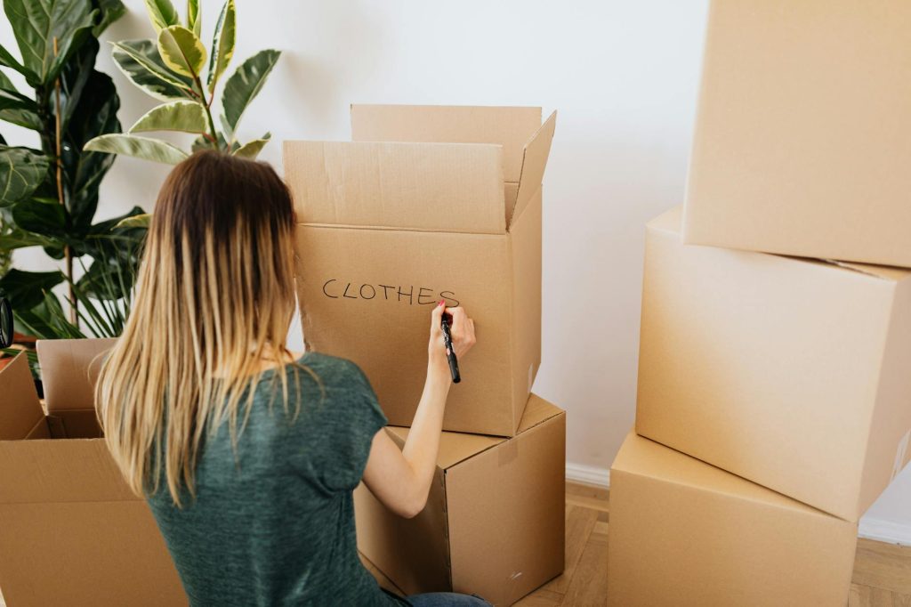 Eco-Friendly House Moving: 5 Effortless Tips Woman labeling cardboard boxes at home, preparing for a move.