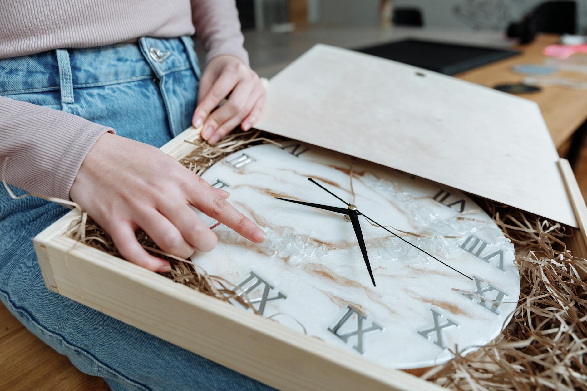 Luxury Cars: 5 Essential Tips for Safe Shipping Hands gently inspecting a resin wall clock with Roman numerals in a wooden box, highlighting craftsmanship.