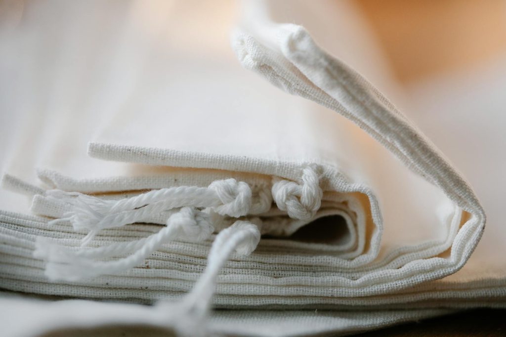 Salvaged Materials: 5 Transformative Ways for Your New Home Pile of folded white cotton bags with ropes made of ecological cloth placed on table in light room on blurred background