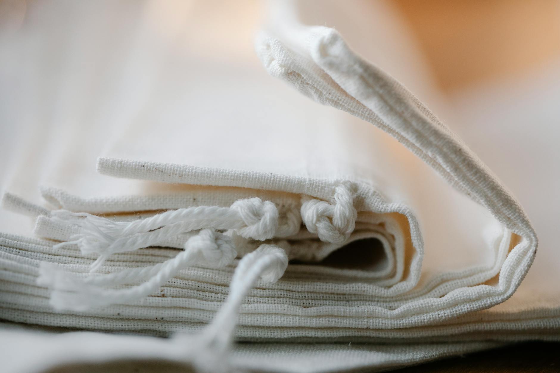Salvaged Materials: 5 Transformative Ways for Your New Home Pile of folded white cotton bags with ropes made of ecological cloth placed on table in light room on blurred background