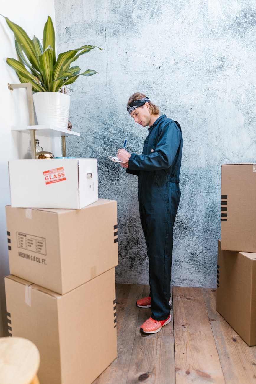 Efficient Industrial Warehouse Relocation Hacks: Must-Try Tips A Caucasian mover in coveralls packing and organizing cardboard boxes indoors.