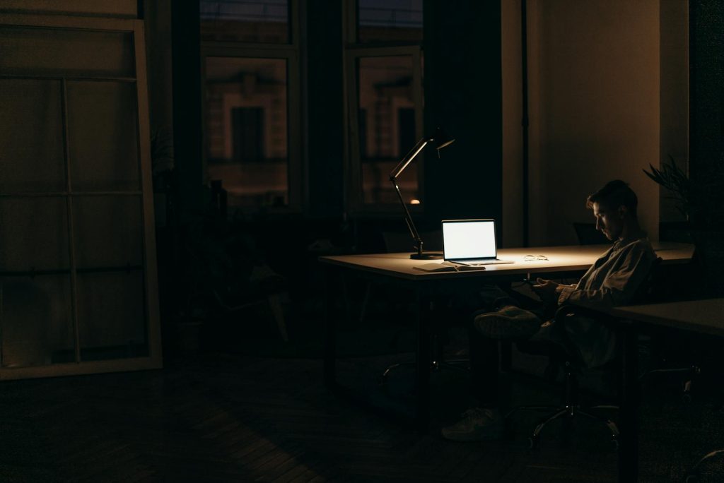 Office Moves Made Effortless: 6 Must-Have Hacks A man working late at night in a dimly lit office, with a bright laptop screen.