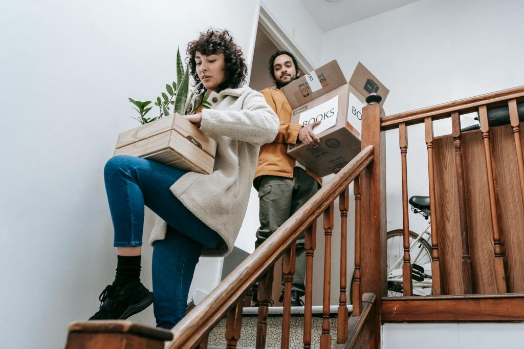 Home Relocation Made Effortless: 6 Essential Steps Couple carrying boxes and plants down stairs during a home move.