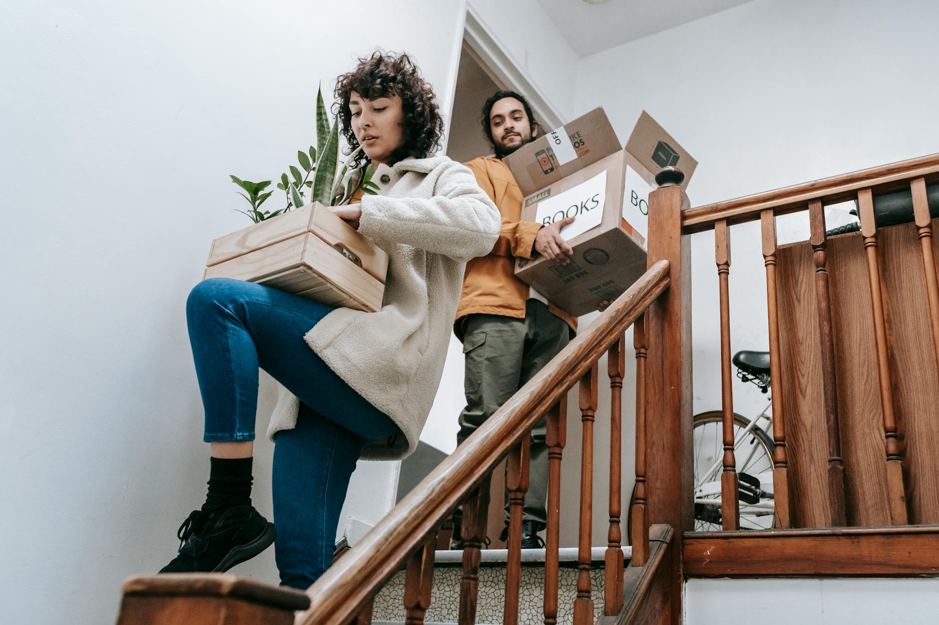 Home Relocation Made Effortless: 6 Essential Steps Couple carrying boxes and plants down stairs during a home move.