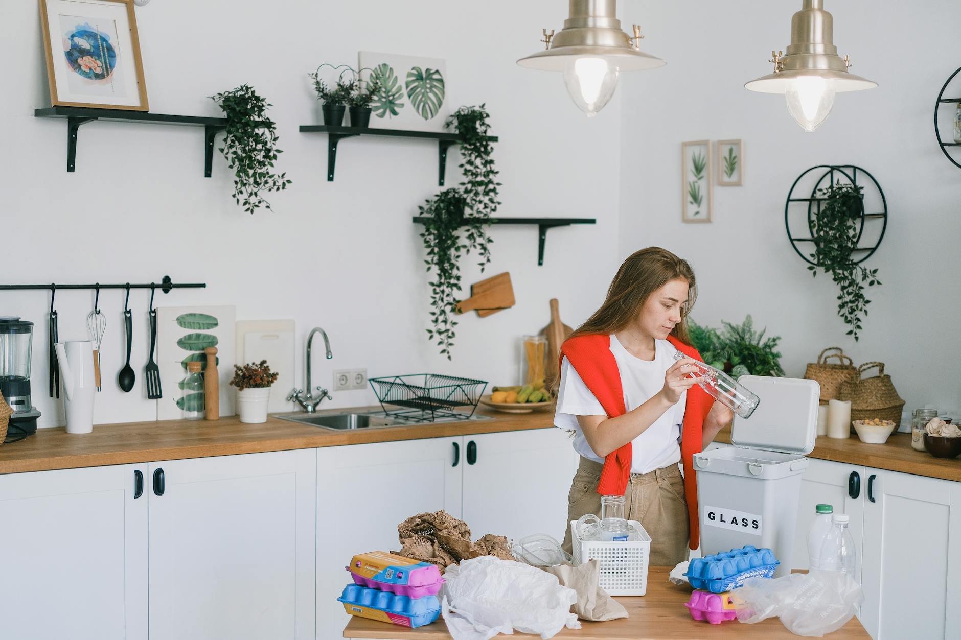 Home Move Hacks: Effortless Waste Reduction in 6 Simple Steps Woman organizing recyclables in a contemporary kitchen setting, promoting eco-friendliness.