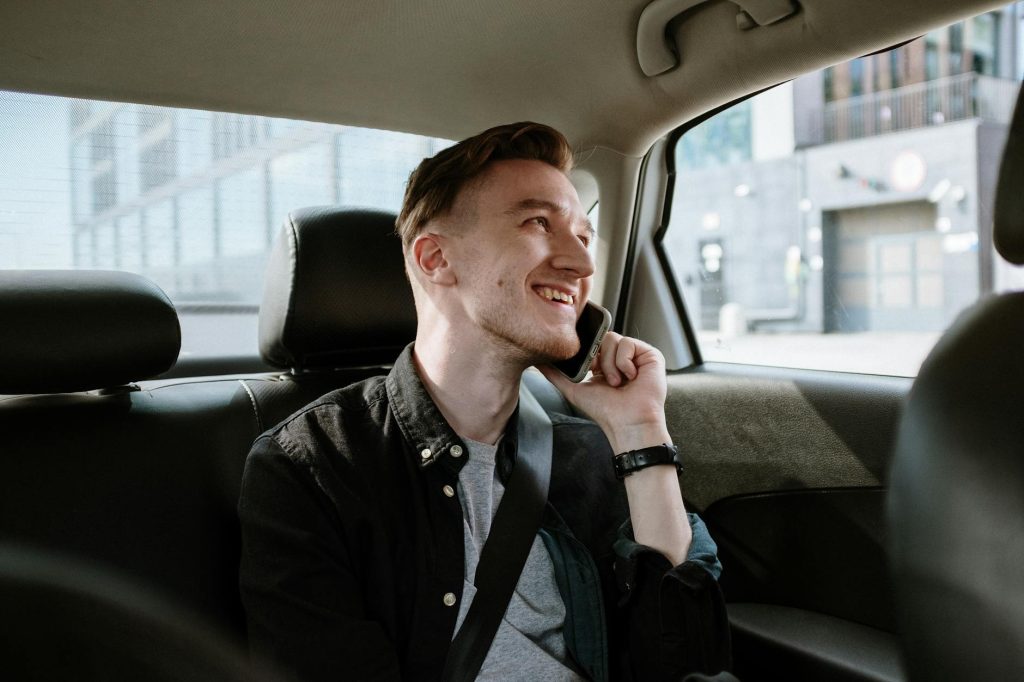 Best Car Transport Service: Top Tips for Effortless Selection Smiling young man enjoying a phone call while seated in the back seat of a car during a daytime ride.