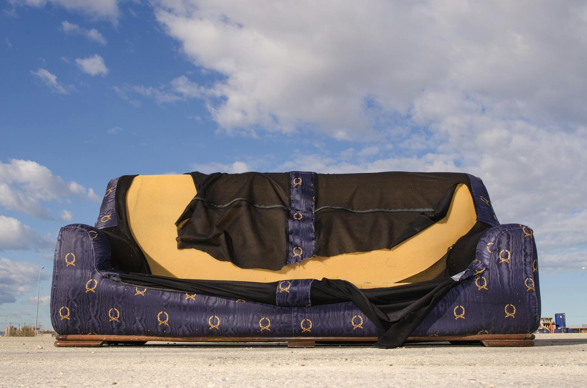 Responsible Furniture Disposal: Effortless Tips for Eco-Friendly Removal A worn-out sofa left on an empty urban street, highlighted against a blue sky with clouds.