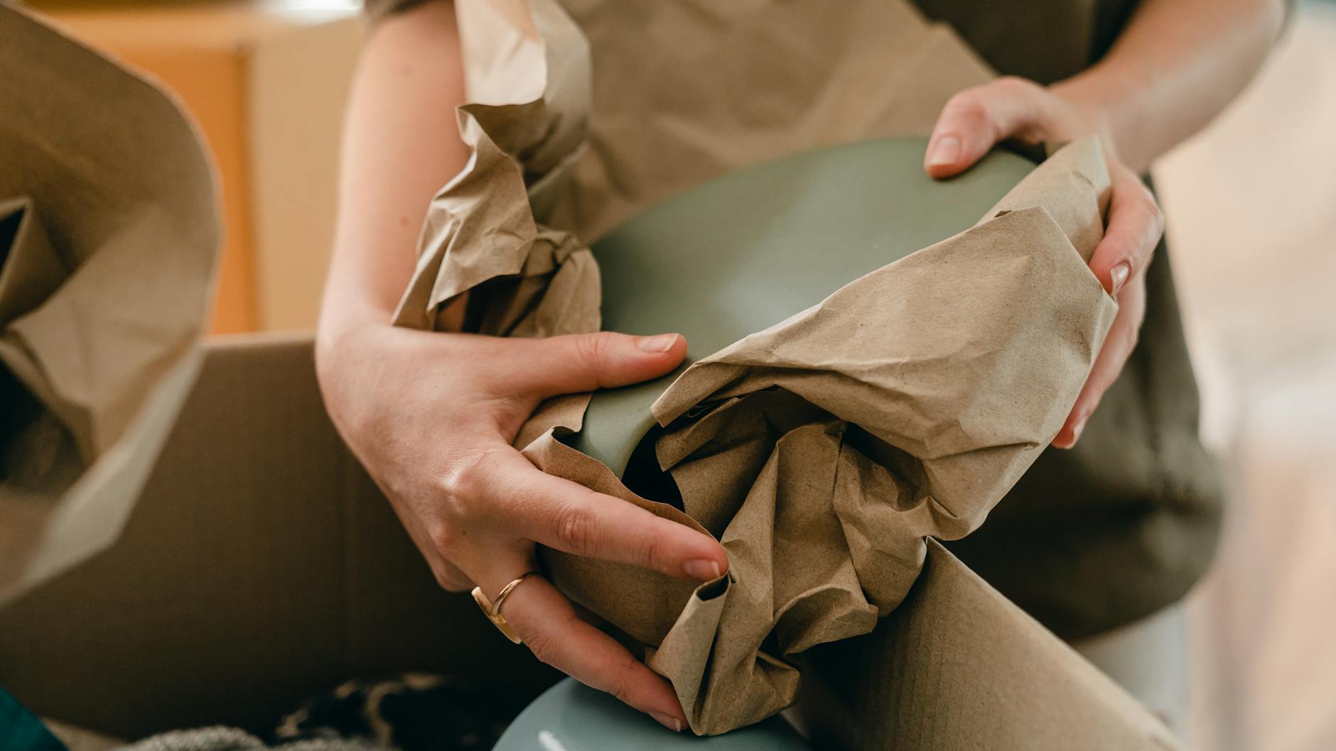 Safe Home Move: Effortless Guide to Packing Fragile Items Hands of a woman carefully wrapping household items in paper while packing a moving box.