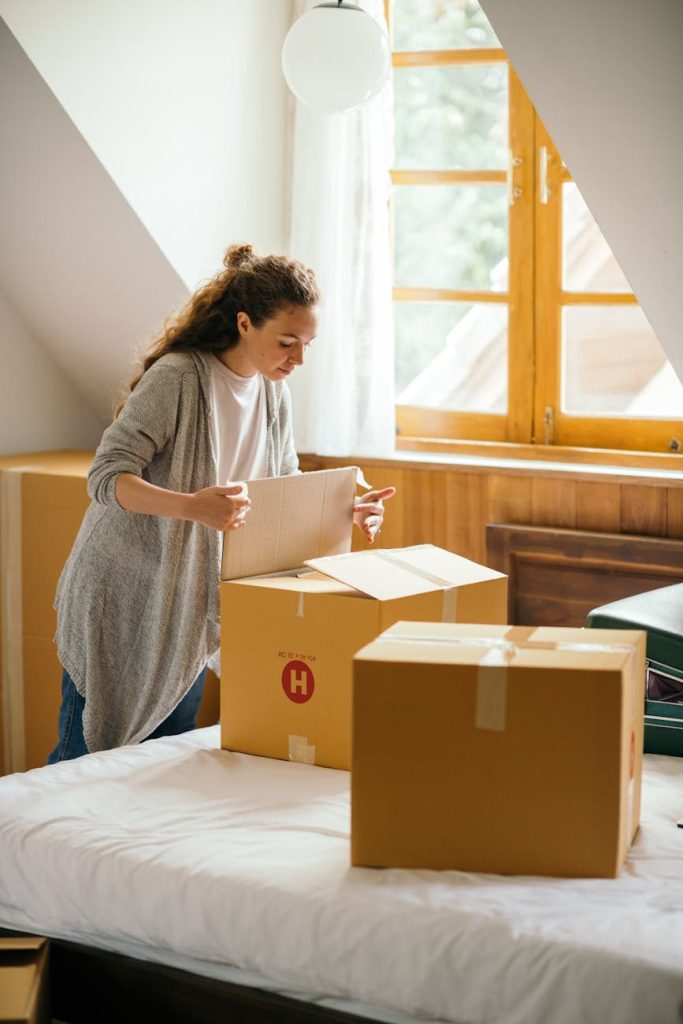 Affordable Tips for Planning a Long-Distance House Move Serious female with curly hair carefully packing stuff in boxes preparing for moving out light apartment