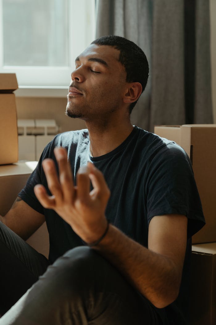 Menus Man practicing meditation in a calm setting surrounded by moving boxes in his apartment.