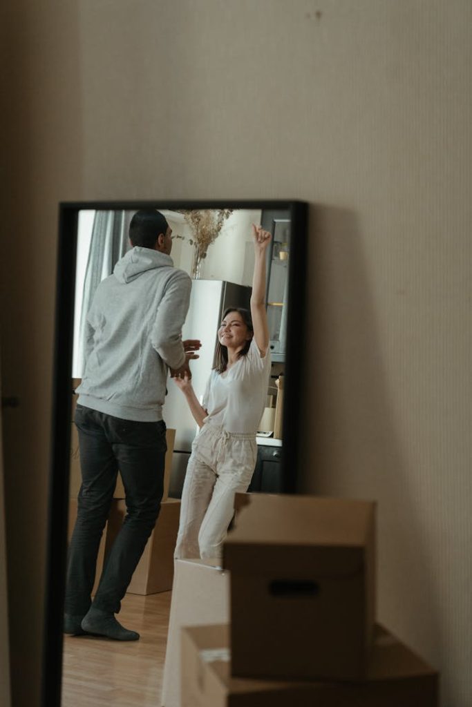 Crafting Captivating Headlines: Your awesome post title goes here Couple happily dances in their new home surrounded by moving boxes, reflecting joy in the mirror.